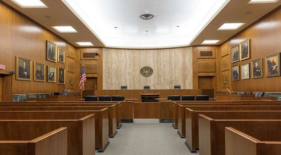 Courtroom inside the historic E. Barrett Prettyman Federal Courthouse, Washington, D.C. Interior of the E. Barrett Prettyman Federal Courthouse courtroom in Washington, D.C., showing wooden benches, judge’s bench with U.S. seal above, American flag, and portraits of legal figures on the walls