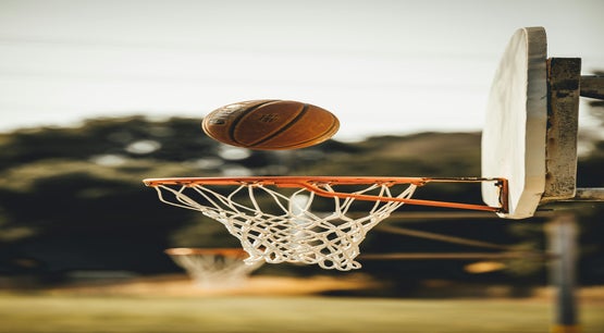 A basketball hovering above an outdoor hoop and net against a blurred tree background