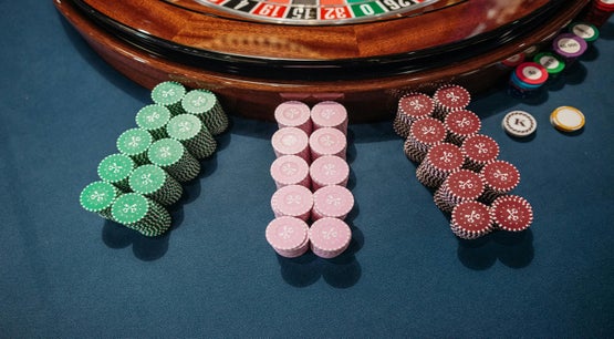 Ontario Online Gaming Market Hits 91% Channelization Stacks of green, pink, and red casino chips arranged on a blue felt surface in front of a roulette wheel