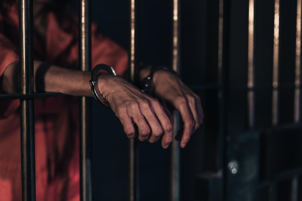Handcuffed person in orange prison uniform behind bars